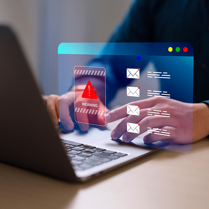 Person using a laptop with a digital email inbox overlay and a red warning alert, representing phishing, spam, or cybersecurity threats.